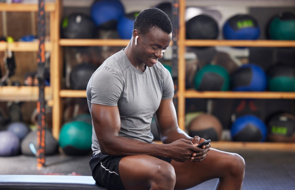 Phone, fitness and black man in gym training, workout or exercise social media or internet search f